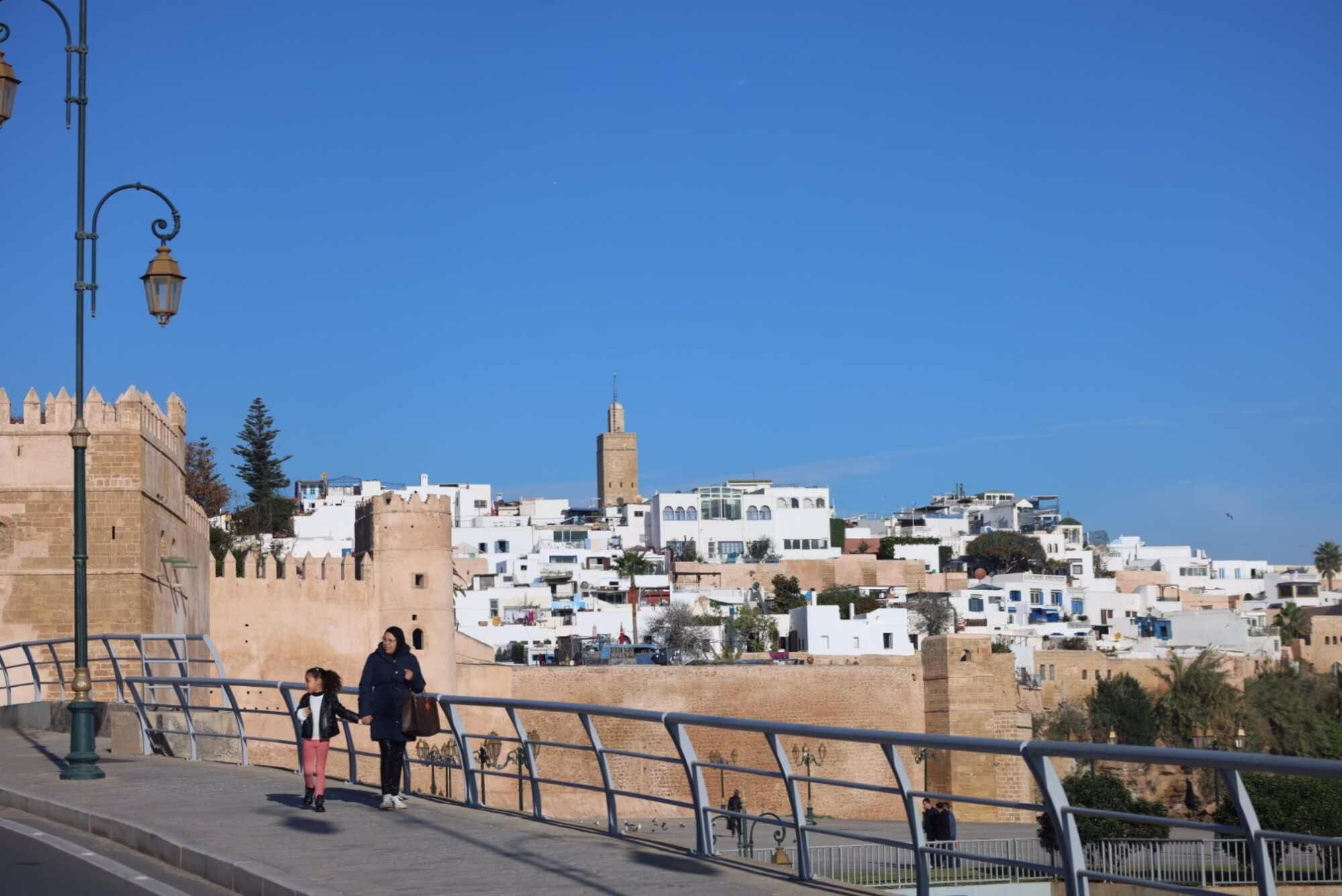 The image is for the Kasbah of Oudayas in Rabat. The image also shows a lady walking with her daughter in the back side of the Kasbah during our Morocco travel package - Morocco holiday - Morocco tour package - Morocco trip package - 10 day Morocco travel package from Casablanca