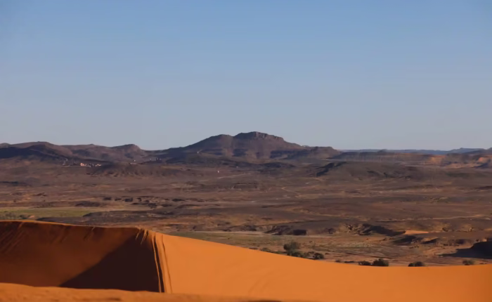 Panoramic view from the top Erg Chabbi Sand dunes show a good contrast of the black rocky desert and the orangey color of the sand - Morocco travel package - Morocco tour package - Morocco holiday - Morocco vacations - Morocco vacation packages - Tangier excursions